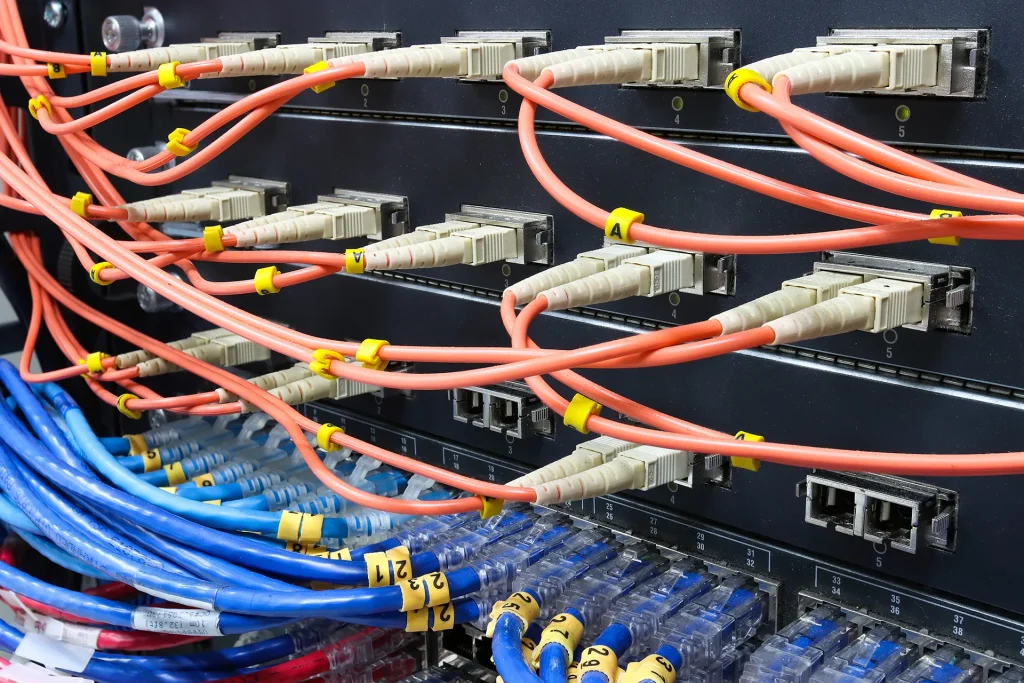 Close-up of a network switch with orange fiber optic patch cables and blue ethernet cables plugged into the ports