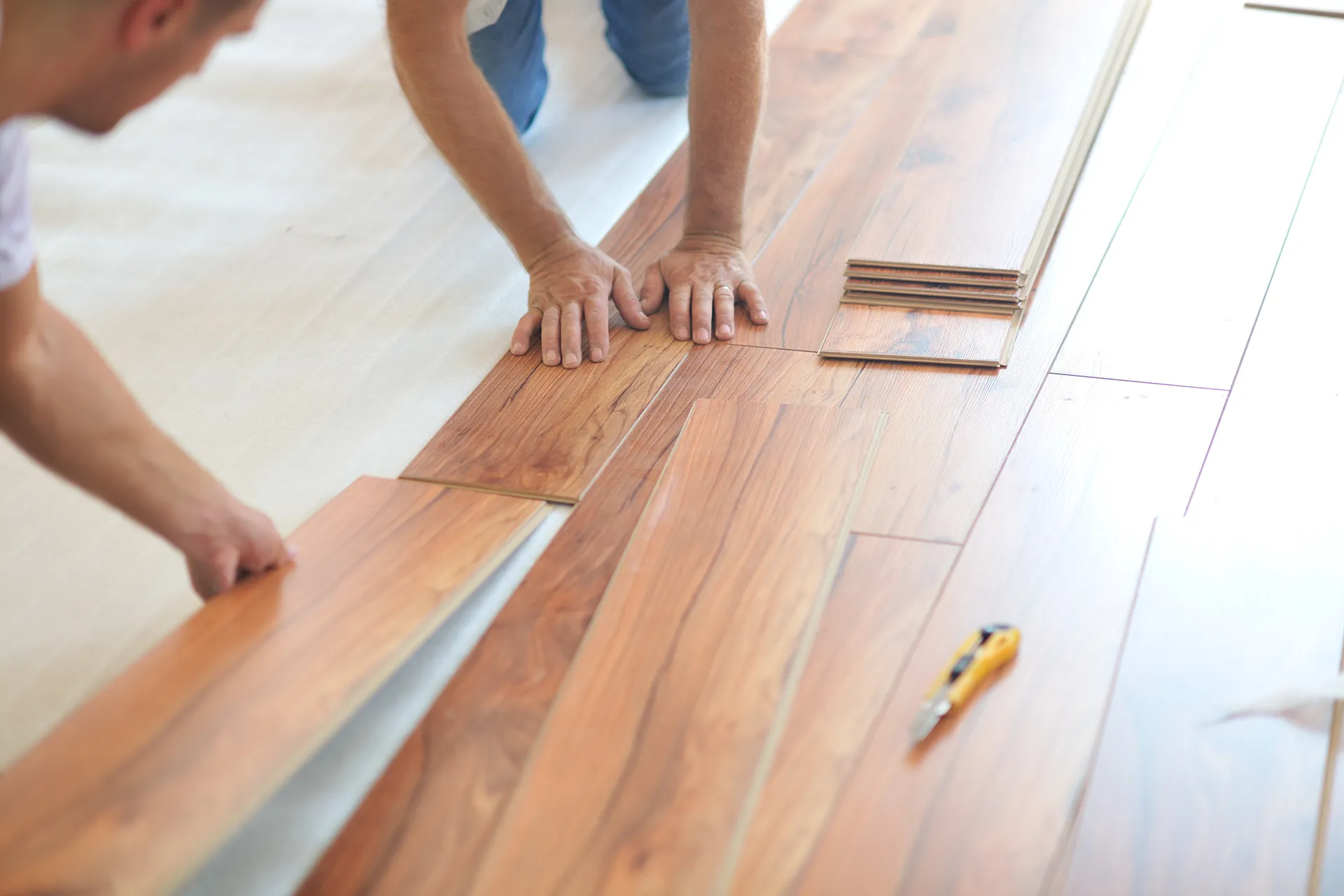 Close-up of hands installing tongue and groove laminate flooring in a home renovation project.